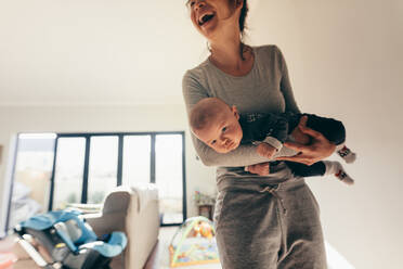 Glückliche Mutter, die mit ihrem Baby im Zimmer ist. Frau, die ihr Baby in den Armen hält und lachend zu Hause steht. - JLPSF21792