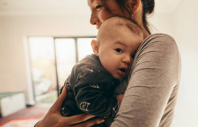 Seitenansicht einer Mutter, die mit ihrem Baby in ihrem Zimmer steht. Nahaufnahme einer glücklichen Mutter, die ihr Baby zu Hause an ihrer Brust hält. - JLPSF21794