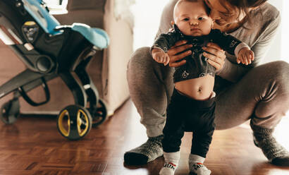 Frau, die ihr Baby von hinten hält und auf dem Boden hockt. Mutter, die ihr Baby verwöhnt und es auf dem Boden laufen lässt. - JLPSF21799