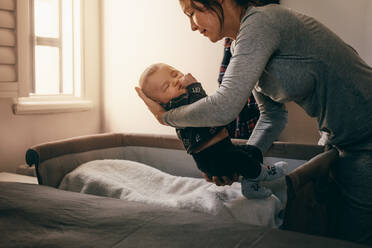 Frau beugt sich vor, um ihr Kleinkind in einen Stubenwagen zu legen. Mutter hält ihr schlafendes Baby, um es auf sein Bett zu legen. - JLPSF21807
