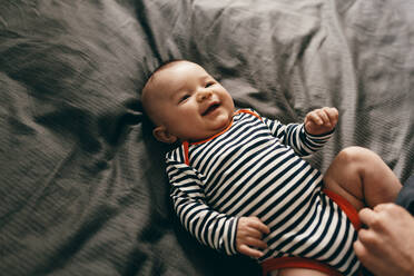 Draufsicht auf ein lächelndes Kleinkind im Bett liegend. Fröhliches kleines Baby in spielerischer Stimmung im Bett liegend. - JLPSF21812