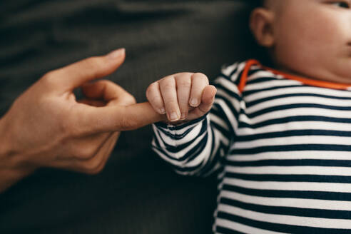 Ein Baby, das den Finger seiner Mutter im Bett hält. Ein Baby, das sich sicher fühlt, indem es einen Finger seiner Mutter hält. - JLPSF21814