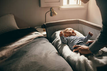 Woman attending to her crying baby trying to pacify him. Mother putting her baby to sleep in his bassinet. - JLPSF21821