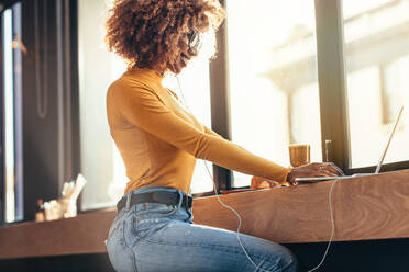 Seitenansicht einer lächelnden afroamerikanischen Frau, die an einem Laptop arbeitet, während sie in einem Café sitzt. Eine Unternehmerin, die ihre Arbeit an einem Laptop in einem Restaurant erledigt. - JLPSF21861