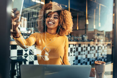 Frau Freiberufler sitzt in einem Café ein Selfie auf dem Handy mit einem Laptop vor. Lächelnde afroamerikanische Frau tut einen Videoanruf auf dem Handy sitzen in einem Restaurant. - JLPSF21866