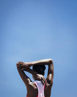 Rückansicht einer Frau beim Dehnen der Armmuskeln vor blauem Himmel im Freien. Fitness-Frau beim Aufwärmtraining im Freien. - JLPSF21894