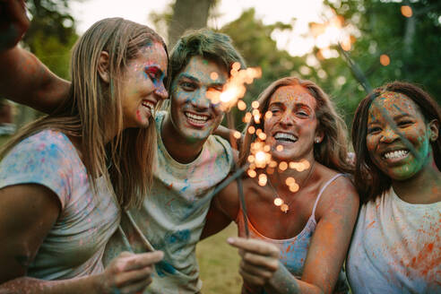 Freunde haben Spaß beim Spielen mit Feuerkerzen, während sie in einem Park Holi spielen. Freunde genießen Holi mit Feuerkerzen. - JLPSF21912