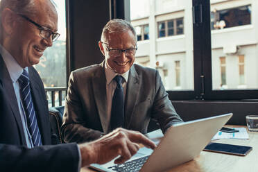 Zwei ältere Geschäftsleute schauen auf einen Laptop auf einem Cafétisch und lächeln. Geschäftspartner arbeiten zusammen in einem Café. - JLPSF21916