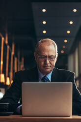 Senior businessman working on laptop while sitting at cafe. Mature caucasian man in suit sitting at cafe working on laptop computer. - JLPSF21918