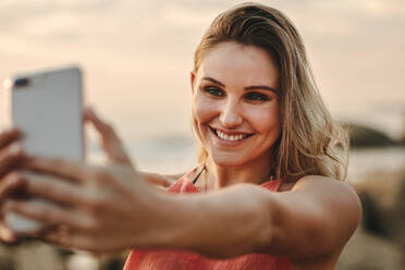 Lächelnde Frau im Urlaub, die ein Selfie mit dem Handy macht. Nahaufnahme einer glücklichen Frau, die ein Handy hält und ein Selfie am Strand macht. - JLPSF21929