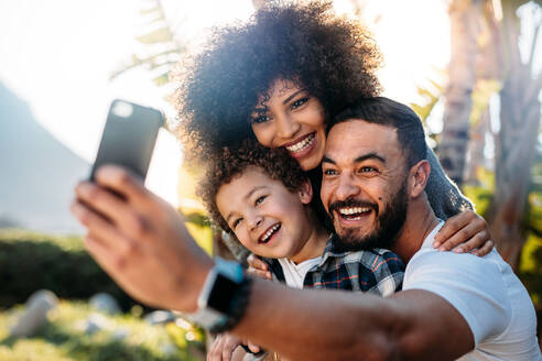 Glückliche Familie posiert für ein Selfie in einem Park an einem sonnigen Tag. Mann macht ein Selfie mit seiner Familie mit dem Handy. - JLPSF21930