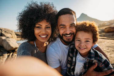 Nahaufnahme eines lächelnden Paares mit einem Kind im Urlaub. Porträt einer Familie, die an einem sonnigen Tag am Strand steht. - JLPSF21934