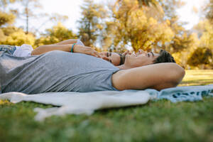 Paar, das sich in einem Park entspannt, auf dem Boden liegt und sich unterhält. Frau schläft auf dem Arm ihres Freundes in einem Park an einem sonnigen Tag. - JLPSF21951