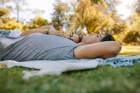 Couple relaxing in a park lying on the ground and talking. Woman sleeping on arm of her boyfriend in a park on a sunny day. - JLPSF21951