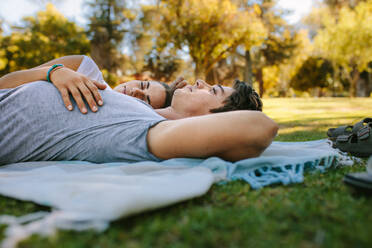 Frau schläft auf dem Arm ihres Freundes in einem Park an einem sonnigen Tag. Glückliches Paar liegt auf dem Boden in einem Park. - JLPSF21952