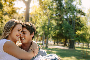 Glückliches verliebtes Paar, das sich in einem Park amüsiert. Ein Mann trägt eine Frau in seinen Armen und geht an einem sonnigen Tag im Park spazieren. - JLPSF21954