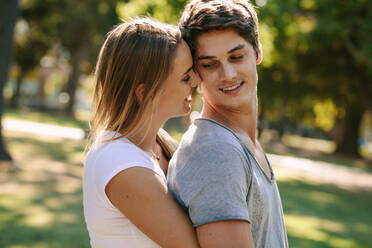 Romantic couple standing in park spending time together. Woman hugging her boyfriend from behind and touching their heads standing outdoors. - JLPSF21957