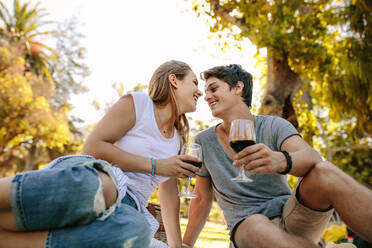 Niedriger Blickwinkel eines romantischen Paares, das in einem Park sitzt, Weingläser hält und sich gegenseitig anschaut. Glückliches Paar beim Picknick in einem Park an einem sonnigen Tag. - JLPSF21964