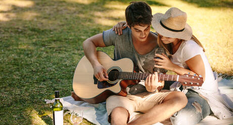 Romantisches Paar sitzt im Park und genießt Musik mit einem Glas Wein. Paar hat Spaß beim Picknick mit Gitarre und Wein. - JLPSF21971