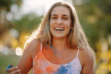 Smiling woman with colours splashed on her body playing holi. Happy woman playing holi with powder colours outdoors. - JLPSF21986