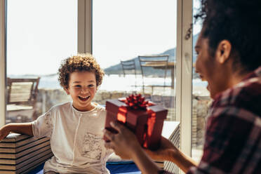 Happy woman giving a gift to her son. Kid excited to see a wrapped gift box in the hands of his mother. - JLPSF21987