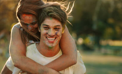 Nahaufnahme eines Paares, das sich beim Holi-Spielen amüsiert. Ein lächelnder Mann trägt seine Freundin auf dem Rücken, während er im Freien Holi spielt. - JLPSF22002