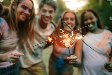 Mann mit Frauen Freunde stehen in einem Park und brennende Feuer funkelt. Gruppe von Freunden genießen Feuerwerk zusammen mit spielen holi. - JLPSF22006