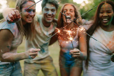 Happy friends having fun burning fire sparkles together after playing holi. - JLPSF22007