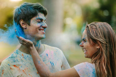 Lächelnde Frau, die einem Mann Farbe aufträgt. Glückliches Paar spielt Holi mit Pulverfarben in einem Park. - JLPSF22008