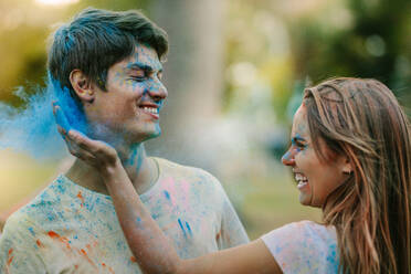 Smiling woman applying colour to a man. Happy couple playing holi with powder colours in a park. - JLPSF22008