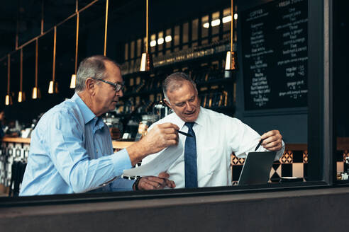 Reife Geschäftsleute schauen auf einen Laptop und besprechen ihre Arbeit in einem Café. Zwei Geschäftspartner treffen sich in einem Restaurant. - JLPSF22012