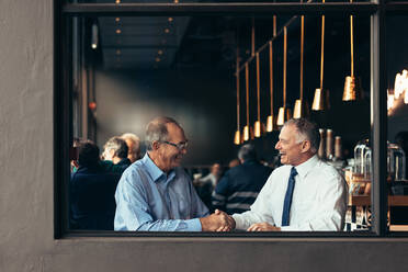 Business people sitting at cafe shaking hands. Two mature business men handshake while sitting at a restaurant. - JLPSF22015