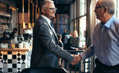 Älterer Geschäftsmann schüttelt einem Mann im Restaurant die Hand. Geschäftsleute treffen sich in einem modernen Café mit einem Händedruck. - JLPSF22020