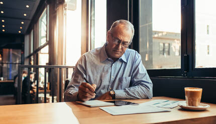 Älterer Geschäftsmann macht sich Notizen, während er im Café sitzt. Älterer Mann arbeitet in einem modernen Café. - JLPSF22026