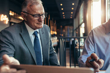 Senior businessman with colleague working at cafe. Businesspeople working together in a restaurant. - JLPSF22027