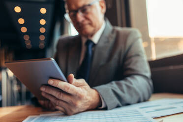 Nahaufnahme eines Geschäftsmannes, der ein digitales Tablet mit Geschäftspapieren auf dem Tisch hält. Geschäftsmann im Café, der an einem digitalen Tablet arbeitet. - JLPSF22034