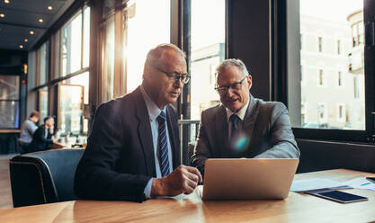 Zwei ältere Geschäftspartner besprechen ein Projekt in einem Café. Ein Geschäftsmann zeigt seinem Partner etwas auf einem Laptop. - JLPSF22040