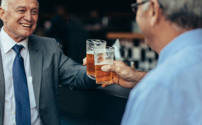 Ältere Geschäftsleute stoßen nach der Arbeit in einer Bar mit Biergläsern an. Geschäftsleute trinken nach der Arbeit in einer Bar. - JLPSF22056
