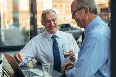 Two senior business professionals having a casual discussing at cafe. Senior businessmen laughing while sitting at cafe with laptop. - JLPSF22060