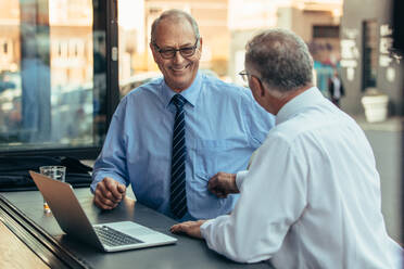 Mature businessmen at cafe counter with laptop discussing work. Senior business professionals having casual talk at cafe after work. - JLPSF22061