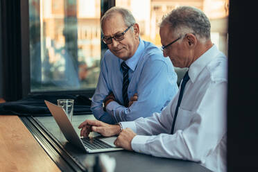Zwei Geschäftsleute arbeiten an einem Laptop in einem Café. Zwei ältere Geschäftsleute schauen in einem Café auf einen Laptop-Computer. - JLPSF22062