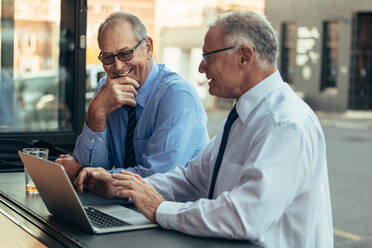 Senior Geschäftsleute im Café mit Laptop diskutieren Arbeit und lächelnd. Senior Business-Profis mit casual diskutieren über Arbeit im Café nach der Arbeit. - JLPSF22063