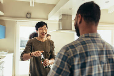 Lächelnder asiatischer Mann, der eine Flasche Bier öffnet und seinen Freund ansieht. - JLPSF22071