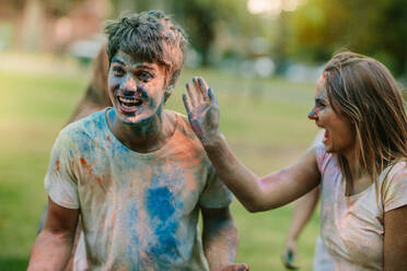 Ein Paar hat Spaß beim Holi-Spielen in einem Park mit Freunden. Eine glückliche Frau genießt Holi, indem sie ihrem Freund Farbe aufträgt. - JLPSF22073