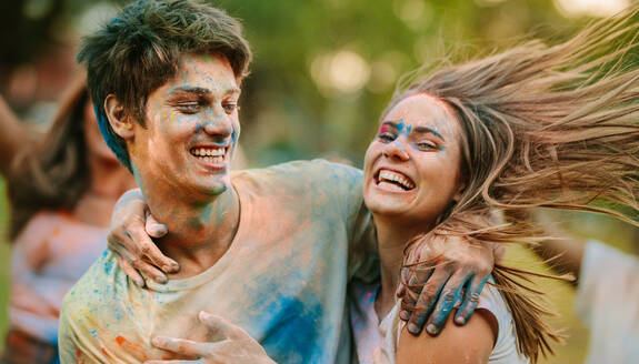 Ein Mann und eine Frau, deren Gesichter mit Holi-Farben verschmiert sind, haben Spaß im Freien. Ein glückliches Paar, das sich gegenseitig hält, spielt Holi mit seinen Freunden in einem Park. - JLPSF22075