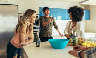 Lächelnde Männer und Frauen, die sich unterhalten und lachen, während sie zu Hause Bier trinken. Freunde, die mit Snacks und Getränken am Esstisch sitzen und Spaß haben. - JLPSF22076