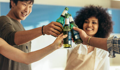 Four friends toasting beer standing together at home. Multiethnic friends at home drinking beer and having fun. - JLPSF22077