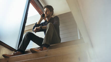 Man sitting on the stairs of his home and talking over mobile phone. - JLPSF22106