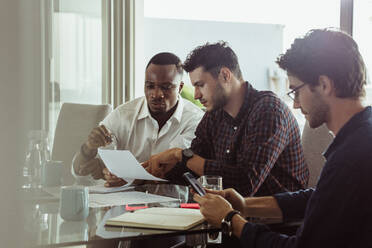 Businessmen discussing work sitting at conference table in office. Two men discussing work while another man is looking at mobile phone. - JLPSF22112