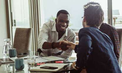 Geschäftsleute besprechen ihre Arbeit am Konferenztisch im Büro. Männer schütteln sich die Hände und lächeln während eines Geschäftstreffens. - JLPSF22113